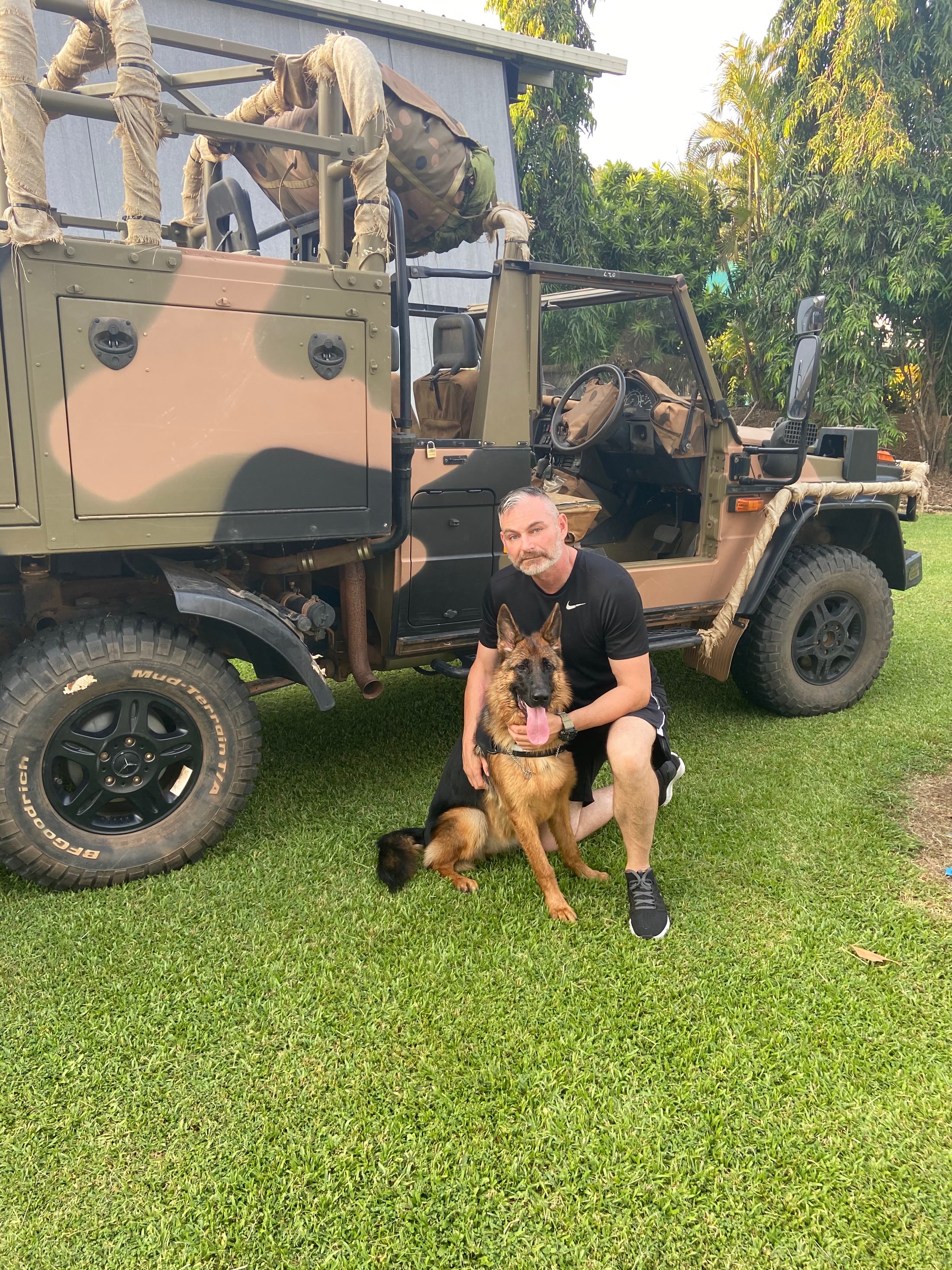 Andy kneeling beside a German shepherd in front of a truck